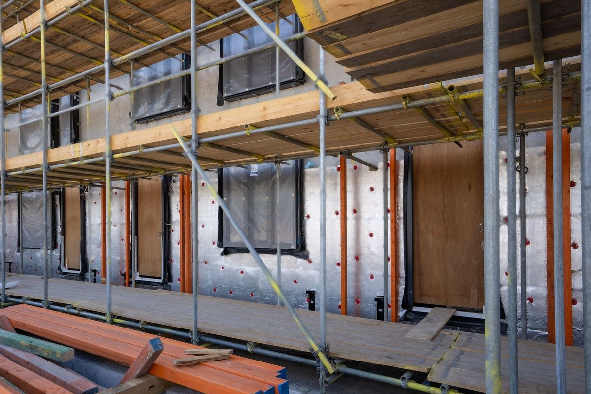 Façade d'un bâtiment en travaux, derrière un échafaudage : paroi recouverte d'une membrane argentée, tasseaux orange